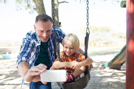 Father taking selfie with son sitting on swing