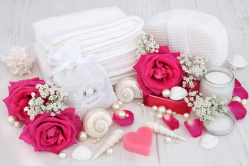 Natural spa beauty cleansing products with pink rose flowers, shells and pearls on distressed white wood  background.