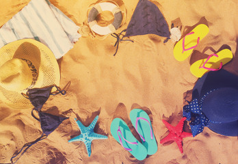 Summer beach fun - flat lay frame on sand with sandals, swimming suits and towels, retro toned