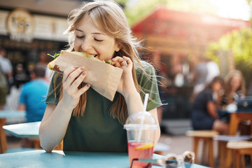 Girl eating taco. Hungry freckled blonde woman eating junk food on a food court on a sunny summer...