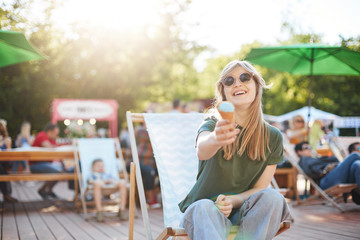 Girl eating ice cream laughing. Portrait of young woman sitting in a park on a sunny day eating icecream looking on camera wearing glasses enjoying summer proposing to camera. Summer lifestyle concept
