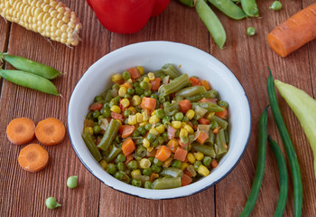 Mexican food stewed vegetables: carrots, green peas, asparagus, sweet peppers, corn. Organic vegetables on a wooden background.