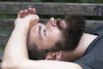 Obraz premium Handsome bearded guy resting laying on a bench in park