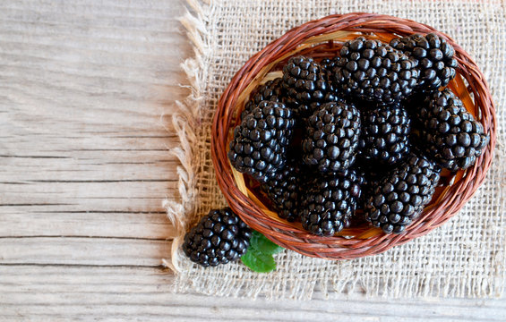 Ripe blackberries in a basket on burlap cloth on old wooden background.Blackberry.Healthy food or diet concept.Selective focus.