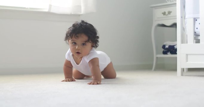 Baby Crawls Toward Rack Focus Low Angle Slow Motion. Baby crawls toward the camera in slow motion smiling and laughing in a white room
