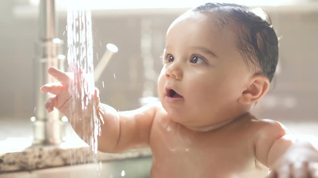 Baby in Awe of Water Stream from Sink Faucet. a stream of water pouring out of the faucet and baby looks at the water in amazement slow motion
