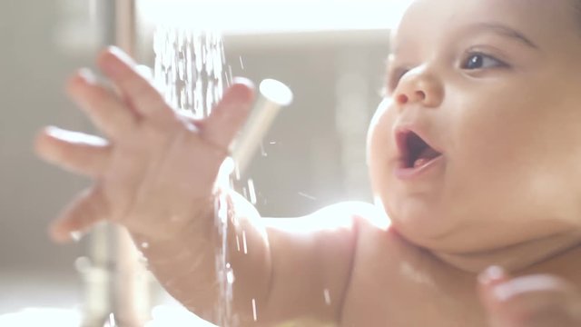 Baby in Sink Bathing and Playing with Water Laughing. close up of baby playing in sink with water from faucet in slow motion
