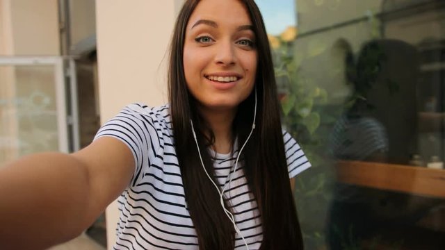 Attractive young woman video cahtting, skyping. Woman waving at the camera while sitting outdoors inh the cafe. close up