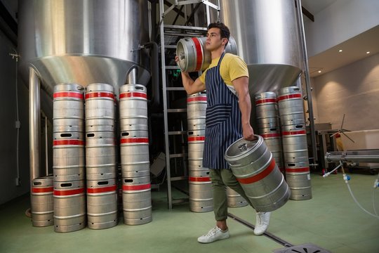 Full length of worker with kegs walking at warehouse