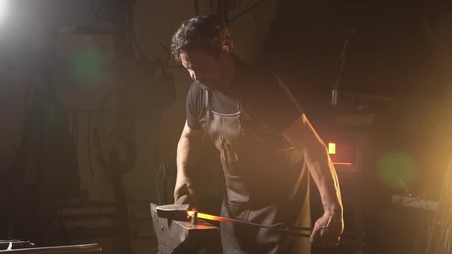 Portrait of a man busy with hard work. The smith works in a workshop with a preform of molten metal. slow motion