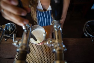 Midsection of barmaid pouring beer from tap in glass