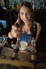 Portrait of beautiful barmaid pouring beer from tap in glass