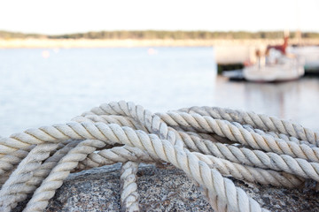 A close up of a dock rope, water surface and coast in the background.
