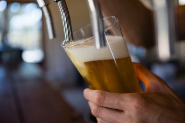 Cropped hand of bartender pouring beer from tap in glass