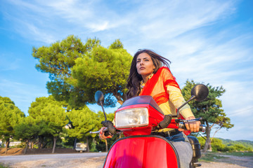 Close up lifestyle image of young fashionable woman in casual outfit sitting on scooter on the street.