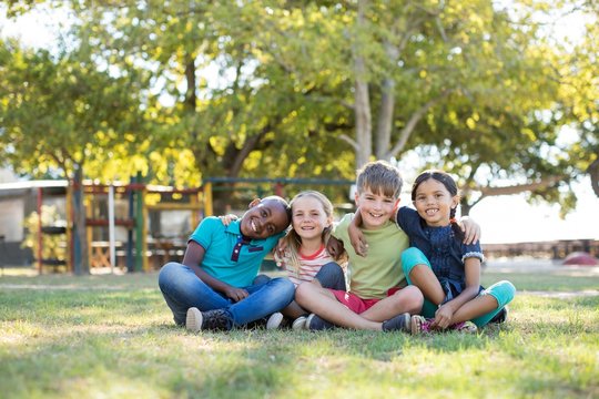 Portrait Of Happy Children With Arms Around Sitting At Park