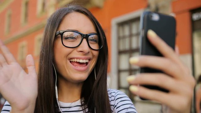 Young caucasian woman in glasses having video chat, skyping on her smartphone outdoors in the street. Video chatting. close up