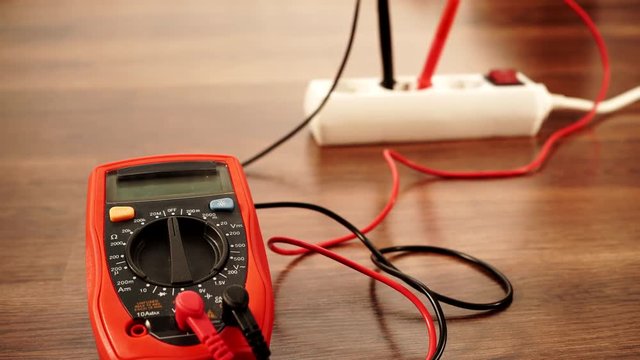 Measurement of voltage in electrical socket extension cord with multimeter on wooden floor background 4K ProRes HQ codec