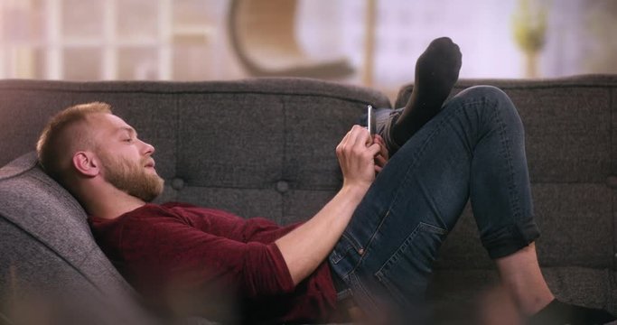 Attractive young boy lying on sofa using tablet