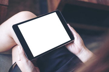 Mockup image of woman's hand holding black tablet pc with blank white screen on thigh in modern cafe