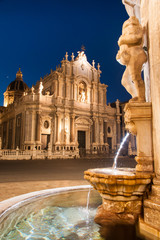 Night view of the fountain at the basis of famous lava stone elephant in the main square of Catania, Sicily, with a view of St. Agatha church