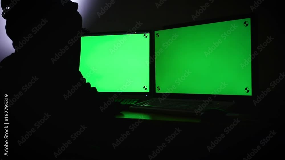 Poster hacker using computer extend green wide screen monitor with motion tracking marker in the dark room 