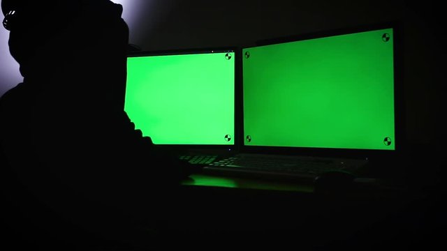 Hacker using computer extend green wide screen monitor with motion tracking marker in the dark room with ambient sound futuristic Technology and cyber criminal concept dark tone processed
