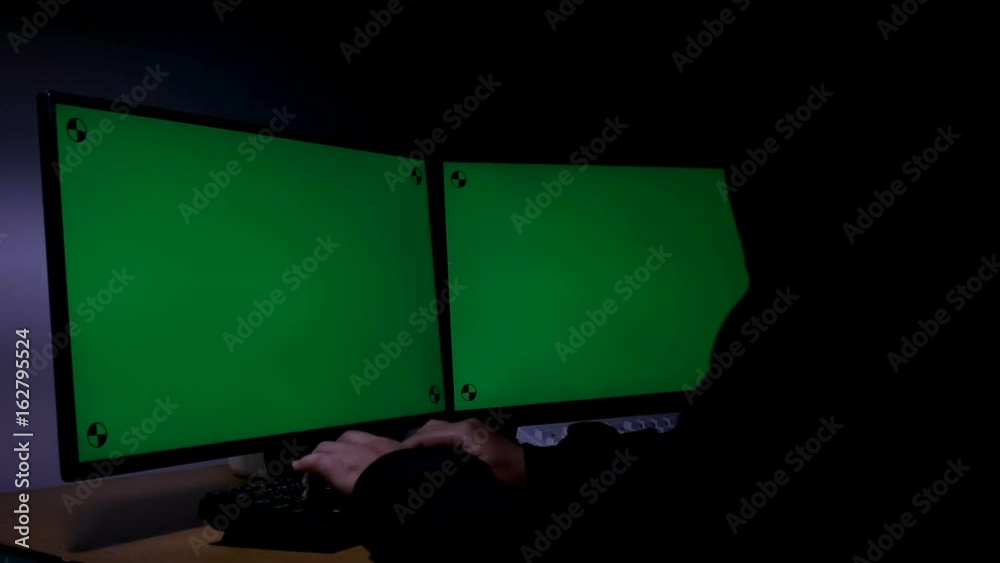 Poster hacker using computer extend green wide screen monitor with motion tracking marker in the dark room 