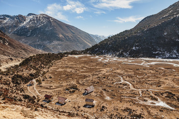 Black mountain with snow on the top and brown mountain with Houses and glacial traces on yellow stone ground at Thangu and Chopta valley in winter in Lachen. North Sikkim, India.