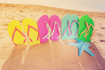 Fototapeta na wymiar Summer beach fun - set of colorful family sandals - green, blue, pink and yellow - in sand, retro toned