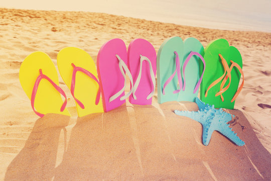Summer beach fun - set of colorful family sandals - green, blue, pink and yellow - in sand, retro toned