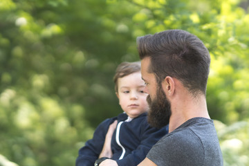 Fototapeta premium Young bearded hipster father holding his little son in park