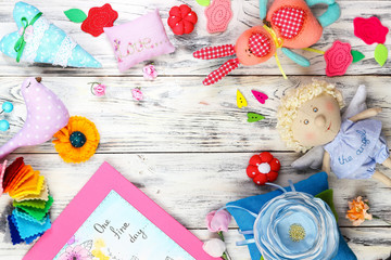 Fototapeta premium Many bright colored soft textile fabulous toys and things handmade greeting card and ceramic plate on white wooden background with copy space Flat lay, top view.