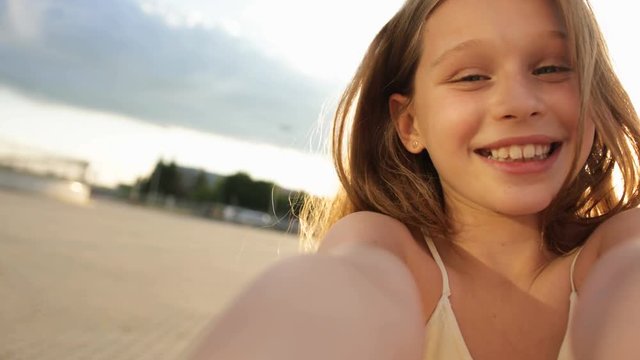 Young girl looks at the camera and twists the camera, smiles in the sunlight