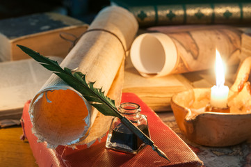 Quill pen, old papers and books by candle light