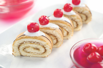 Cakes with cream and cherries on a light background.