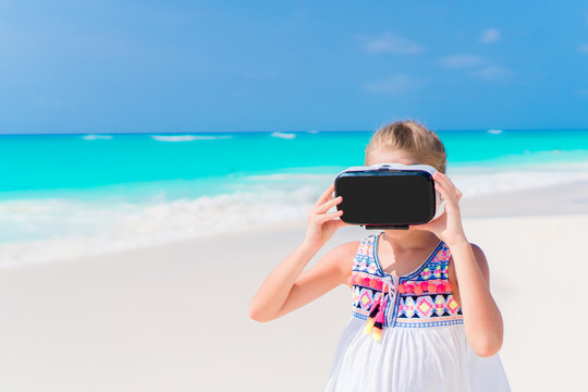 Little girl using VR virtual reality goggles. Adorable kid look into the virtual glasses on white beach