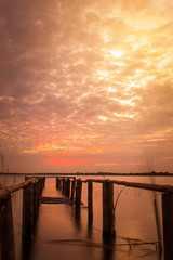 Fototapeta premium long exposure of wooden old bridge into the lake on the background of worm sky sunset.