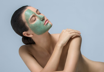 Young woman applaying green face mask - studio portrait