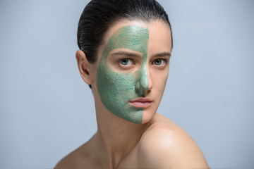 Young woman applaying green face mask - studio portrait