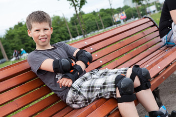 A ten-year-old boy sits on a bench in protective equipment for roller skating