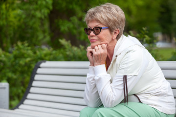 Fototapeta premium Thoughtful European senior woman resting on the bench, looking away, copyspace