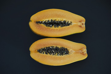 Two halves of ripe papaya fruit with seeds, seen from above with dark blue background