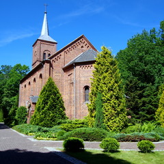 Fototapeta na wymiar Piękny ceglany kościół w małej polskiej wiosce Moja Wola, wraz z przyległym parkiem