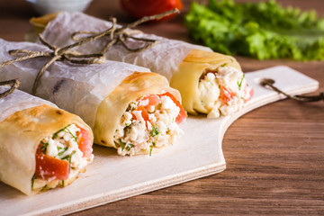 Rolls of pita stuffed with cheese, chicken and tomato  on a wooden table