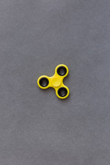 Yellow fidget spinner device on grey background. Top view. Playing with a yellow hand spinner...