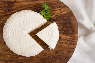 Bovenaanzicht op gesneden ronde witte zelfgemaakte kaas - traditioneel melk romig zuivelproduct op vintage houten bord. Rustieke stijl.