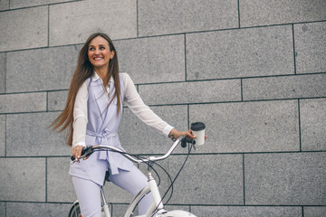 Beautiful young woman on bicycle with coffee. Businesswoman smiling and cycling to work.