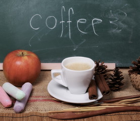 Cup of coffee with cinnamon sticks, apple and chalkboard on jute, linen sack