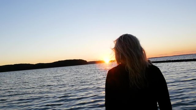 blonde frau am wasser zum sonnenuntergang mit wehenden haaren